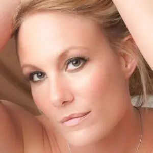 A blond woman posing with her hands on her head.