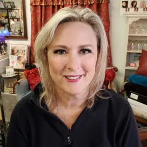 A woman in a black jacket smiling in front of a mirror.