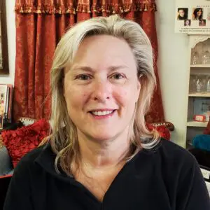 A woman in a black shirt smiling in front of a couch.