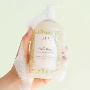 A hand holding a bottle of Farmhouse Fresh Fluffy Bunny Body Wash and Bubble Bath infused with neem oil, drawing on the wisdom of Ayurvedic skin care.