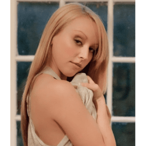 A blond woman posing in front of a window.