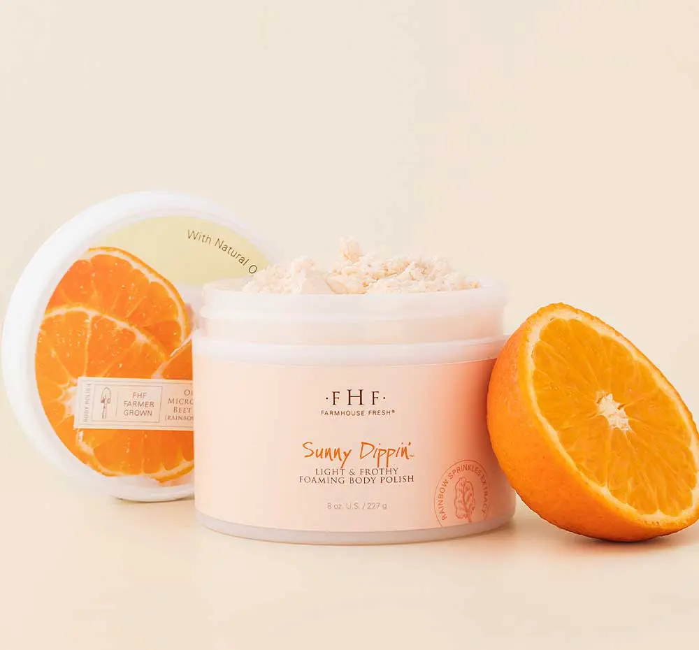 A jar of FHF Sunny Dippin' Foaming Body Polish next to a jar of orange juice.