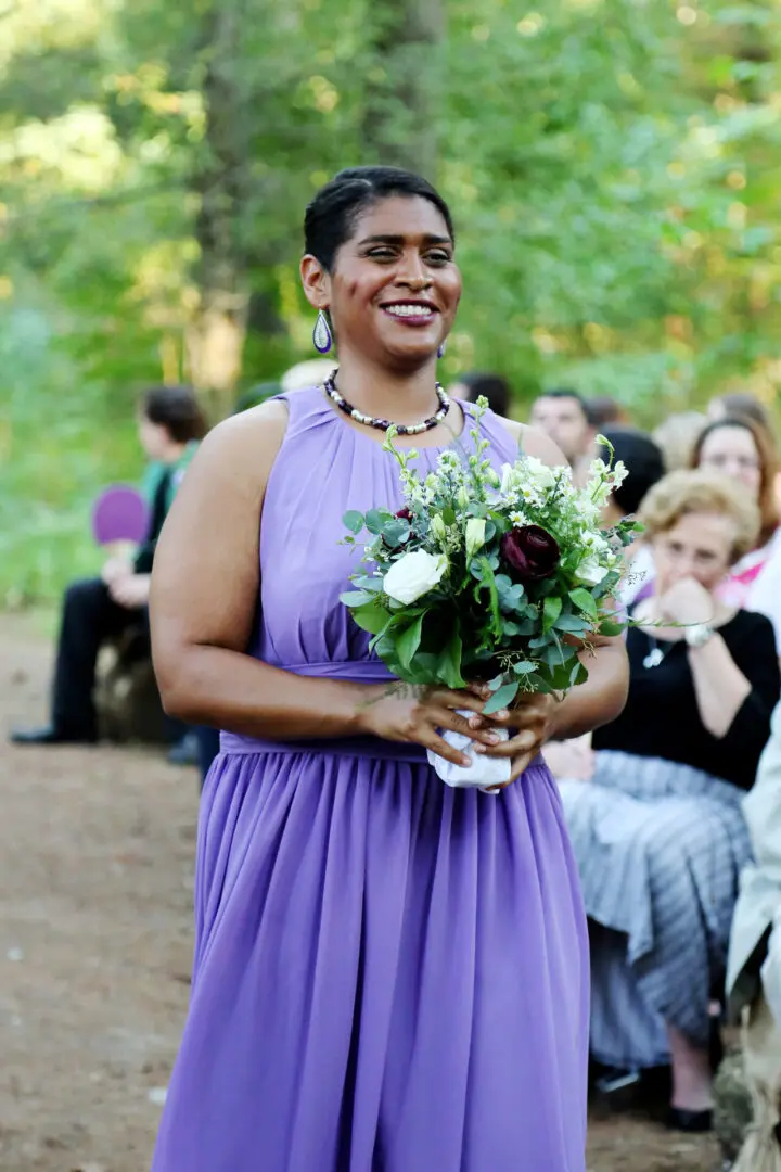Smiling bridesmaid in purple dress holding bouquet.