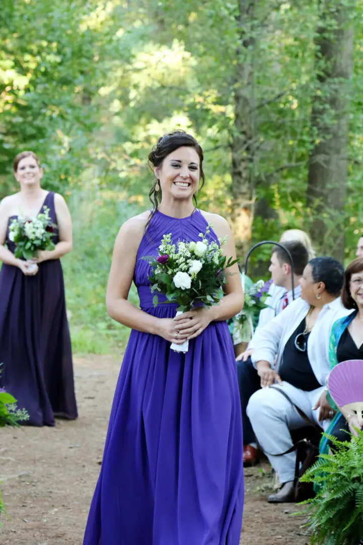 Smiling bridesmaid in purple gown, holding flowers.