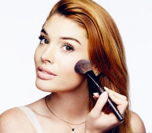 Woman with red hair applying makeup.