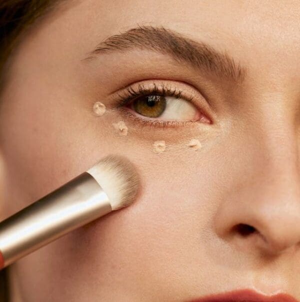 Woman applying concealer with a brush.