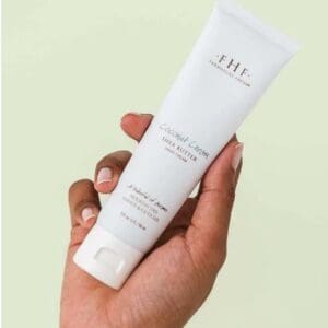 A hand holding a tube of Farmhouse Fresh Coconut Cream Hand Cream (NO BOX SALE).