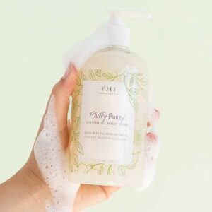 A hand holding a bottle of Farmhouse Fresh Fluffy Bunny Body Wash and Bubble Bath infused with neem oil, drawing on the wisdom of Ayurvedic skin care.