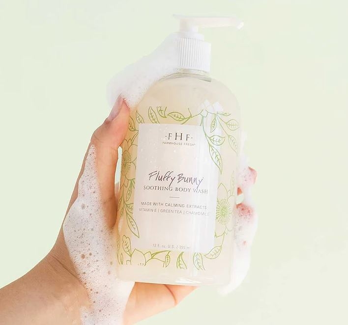 A hand holding a bottle of Farmhouse Fresh Fluffy Bunny Body Wash and Bubble Bath infused with neem oil, drawing on the wisdom of Ayurvedic skin care.