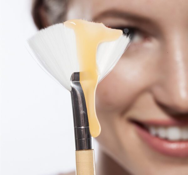 A woman is holding a makeup brush with a yellow liquid on it.