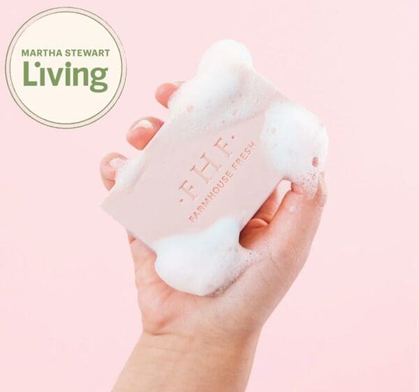 A hand holding a Farmhouse Fresh Pink Moon Shea Butter Soap bar with foam on it.