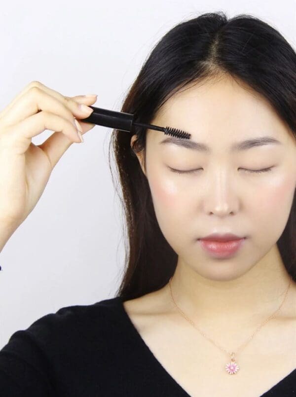 Woman applying eyebrow gel with brush.