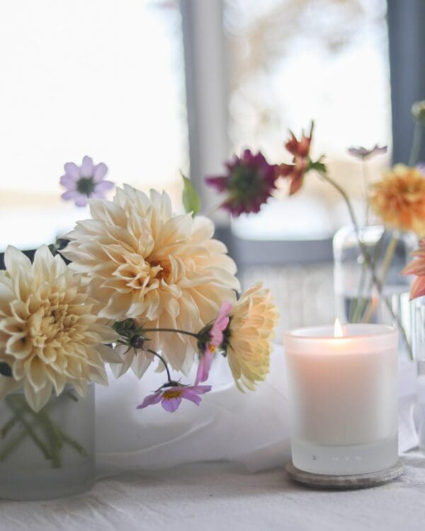 A lit candle with flowers in a vase.