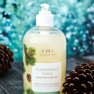 A bottle of Farmhouse Fresh LIMITED Holiday Hand & Body Wash "Wandering Pines" with pine cones next to it.