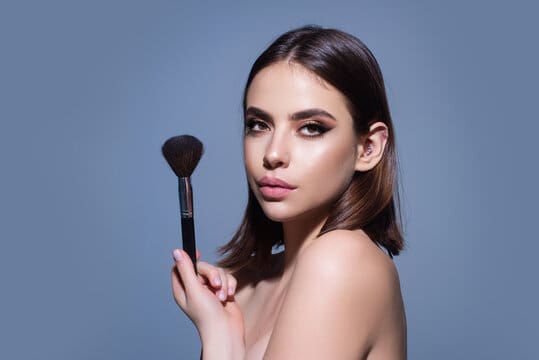 Woman holding makeup brush against blue background.