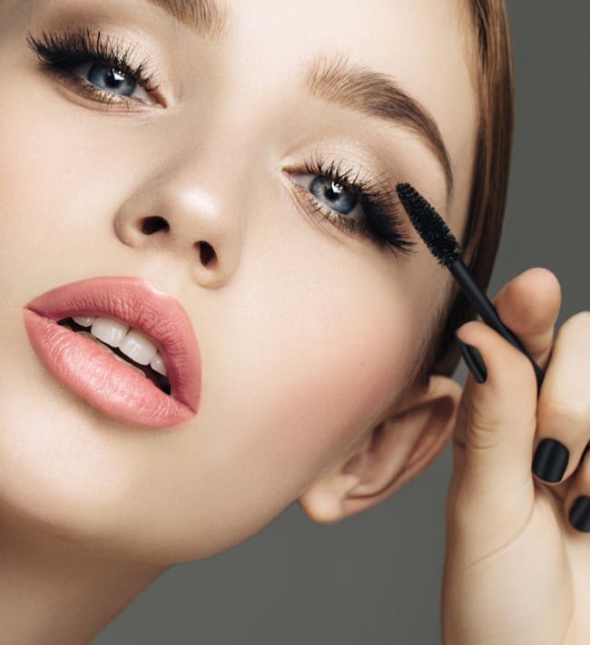 Woman applying mascara to her eyelashes.